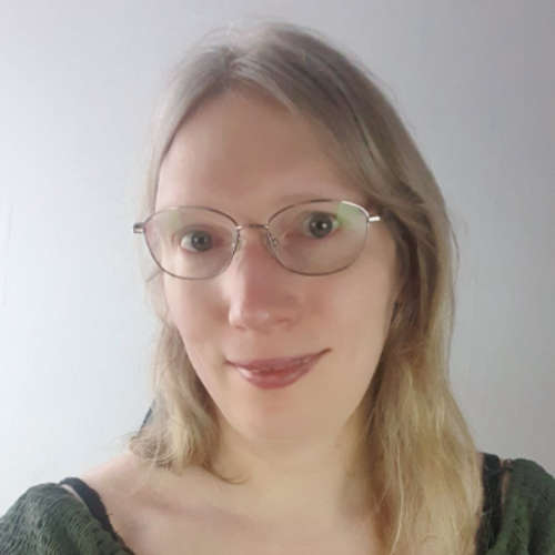 Lea smiling, wearing a dark green dress, with blonde long hair and glasses